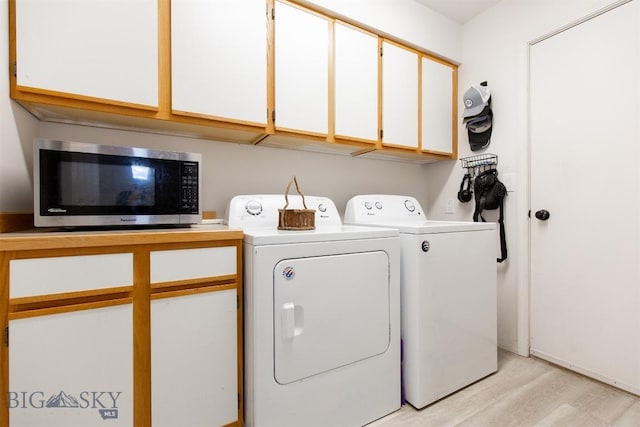 clothes washing area with cabinets, washing machine and clothes dryer, and light wood-type flooring