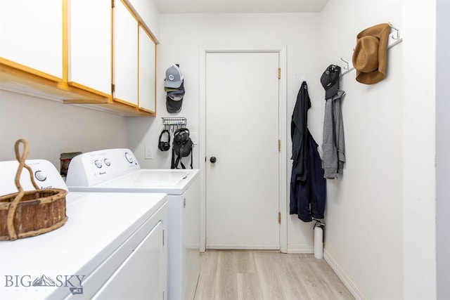 clothes washing area featuring cabinets, washing machine and dryer, and light wood-type flooring