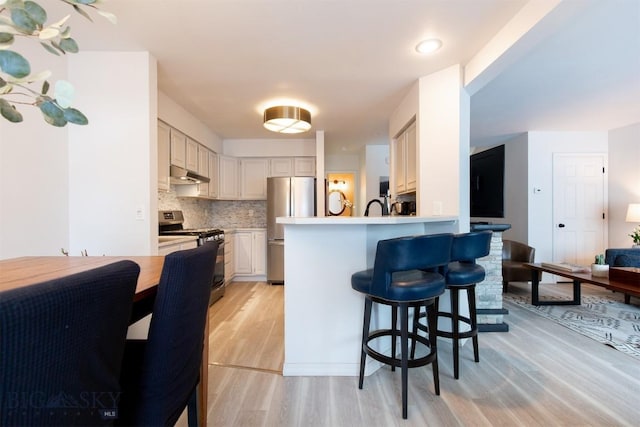 kitchen featuring a breakfast bar, tasteful backsplash, light hardwood / wood-style flooring, appliances with stainless steel finishes, and kitchen peninsula