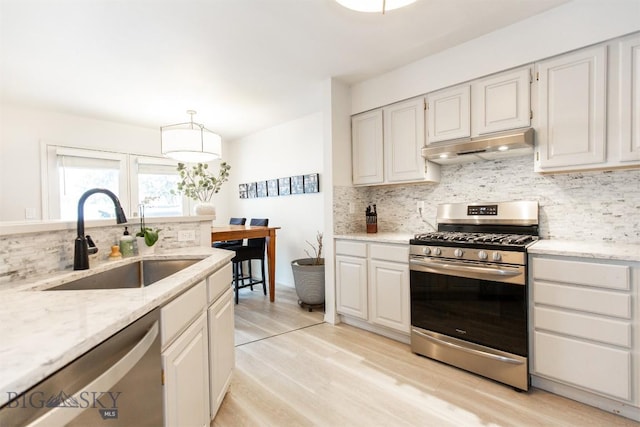 kitchen featuring pendant lighting, sink, stainless steel appliances, light stone counters, and white cabinets