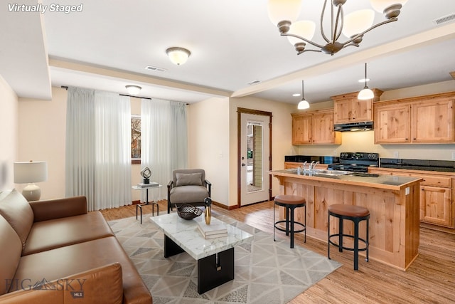 kitchen with black stove, visible vents, light brown cabinets, under cabinet range hood, and a kitchen breakfast bar