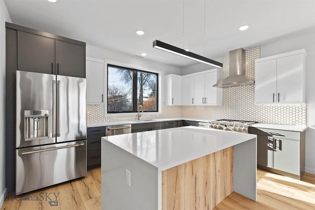 kitchen with sink, a center island, wall chimney range hood, stainless steel appliances, and white cabinets