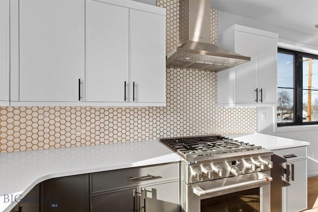 kitchen featuring stainless steel gas stove, white cabinetry, decorative backsplash, and wall chimney exhaust hood