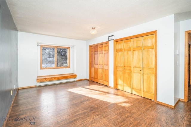 unfurnished bedroom featuring multiple closets, a baseboard heating unit, and dark wood-type flooring