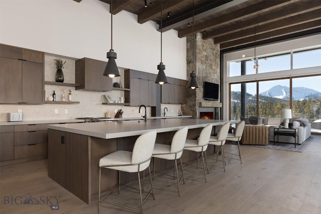 kitchen featuring a kitchen island with sink, beam ceiling, tasteful backsplash, and light hardwood / wood-style flooring