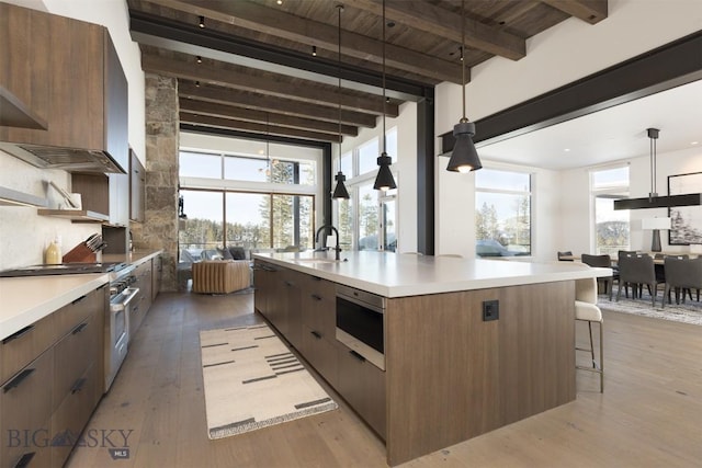 kitchen with decorative light fixtures, high end stove, light hardwood / wood-style floors, beam ceiling, and a spacious island