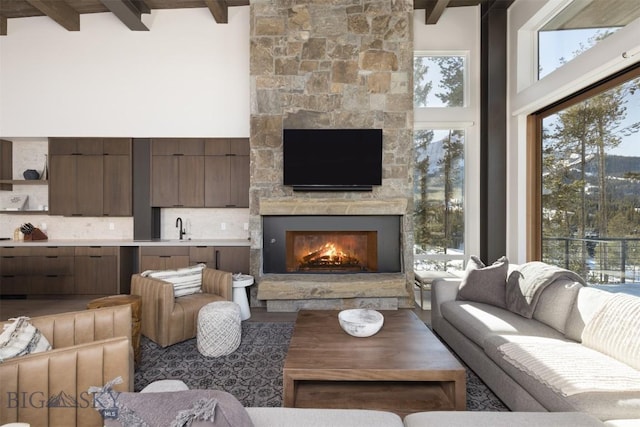 living room with a high ceiling, a stone fireplace, sink, and beam ceiling