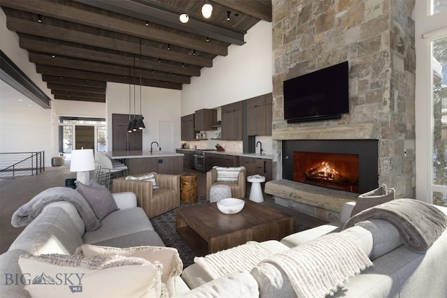 living room with a fireplace, beam ceiling, sink, and a towering ceiling