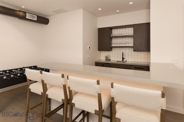 bar featuring dark brown cabinets, sink, and decorative backsplash