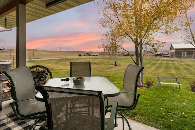 patio terrace at dusk featuring a rural view and a lawn