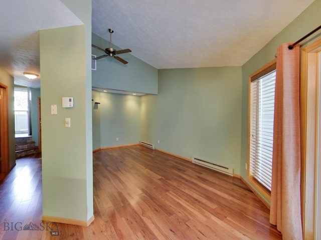 spare room featuring lofted ceiling, a baseboard heating unit, light hardwood / wood-style flooring, and ceiling fan