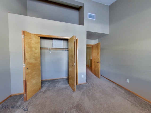 unfurnished bedroom with light carpet, a towering ceiling, and a closet