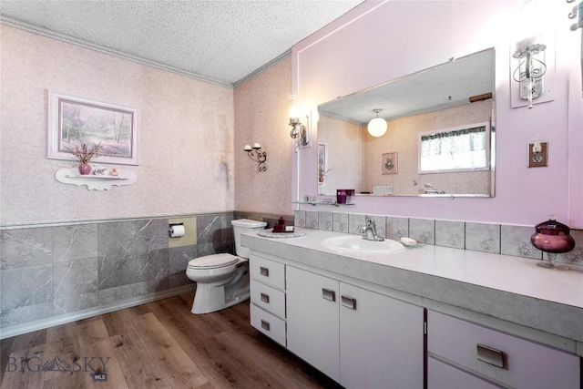 bathroom with wood-type flooring, ornamental molding, vanity, toilet, and a textured ceiling