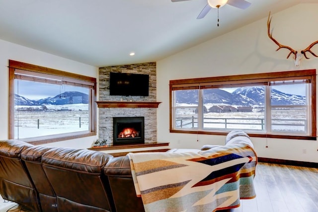 living room featuring ceiling fan, lofted ceiling, a stone fireplace, and light hardwood / wood-style floors