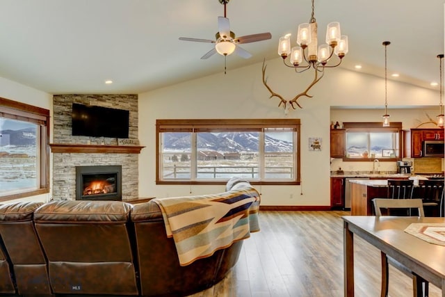 living room with a fireplace, vaulted ceiling, ceiling fan, and light wood-type flooring