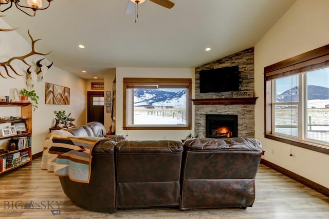 living room with ceiling fan, lofted ceiling, a stone fireplace, and light hardwood / wood-style floors