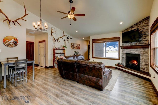 living room featuring high vaulted ceiling, a stone fireplace, ceiling fan with notable chandelier, and light wood-type flooring