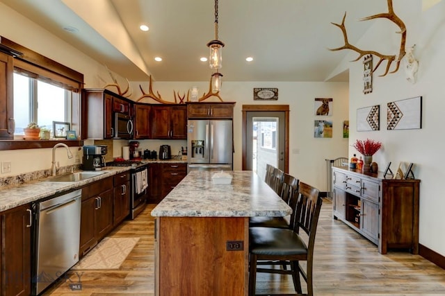 kitchen featuring a kitchen island, appliances with stainless steel finishes, pendant lighting, sink, and light stone countertops