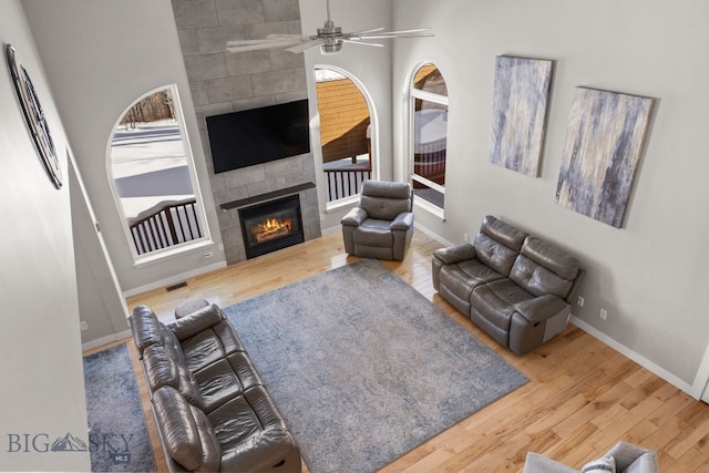 living room with wood-type flooring, a tile fireplace, and ceiling fan