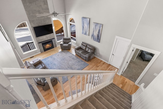 living room featuring a high ceiling, a tile fireplace, hardwood / wood-style flooring, and ceiling fan