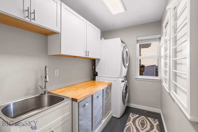 washroom with cabinets, stacked washer and dryer, and sink