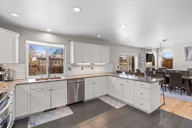 kitchen with white cabinetry, decorative light fixtures, appliances with stainless steel finishes, kitchen peninsula, and light stone countertops