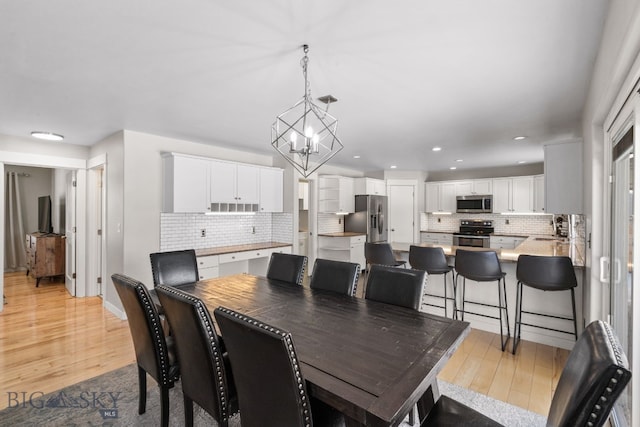 dining room with an inviting chandelier, sink, and light hardwood / wood-style flooring