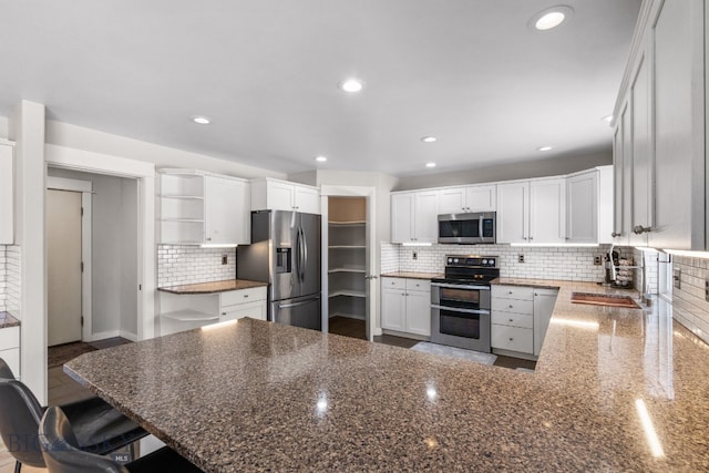 kitchen with sink, dark stone counters, kitchen peninsula, stainless steel appliances, and white cabinets