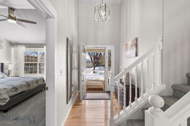 foyer with ceiling fan with notable chandelier, a wealth of natural light, light hardwood / wood-style floors, and a high ceiling