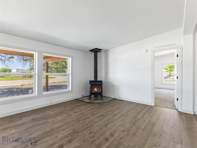 unfurnished living room with wood-type flooring, a textured ceiling, and a wood stove