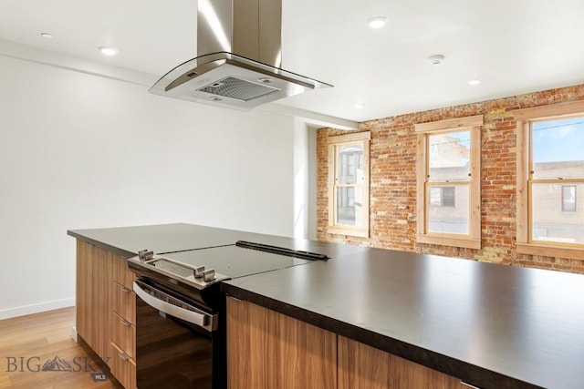 kitchen with range with electric cooktop, brick wall, island range hood, and light hardwood / wood-style flooring