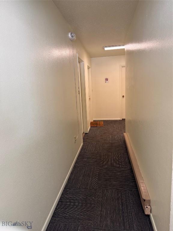 hallway with a textured ceiling and dark colored carpet