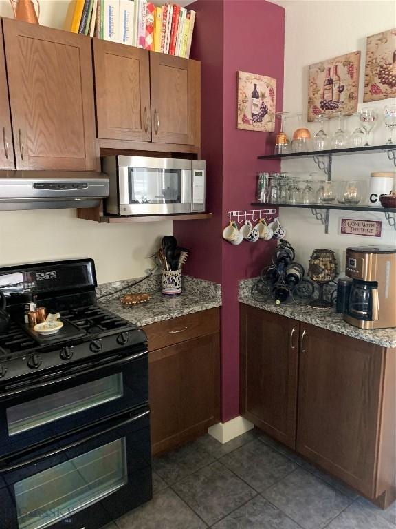 kitchen featuring light stone counters, double oven range, light tile patterned floors, and exhaust hood