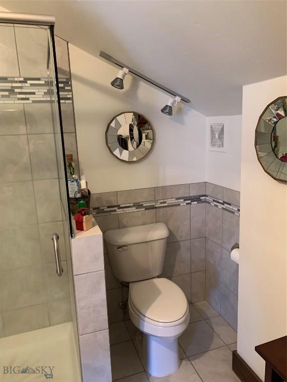 bathroom featuring tile patterned flooring, toilet, tile walls, and walk in shower