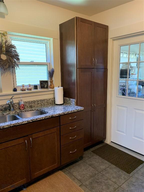 kitchen featuring tile patterned flooring, plenty of natural light, light stone countertops, and sink