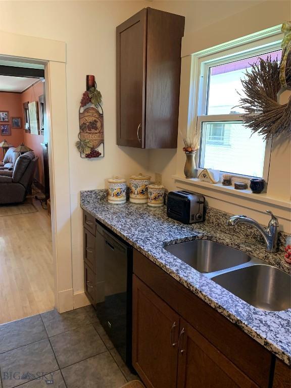 kitchen featuring black dishwasher, sink, dark tile patterned flooring, dark brown cabinetry, and light stone countertops