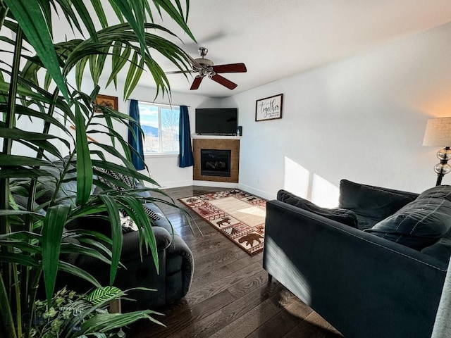 living room with a tiled fireplace, dark hardwood / wood-style floors, and ceiling fan