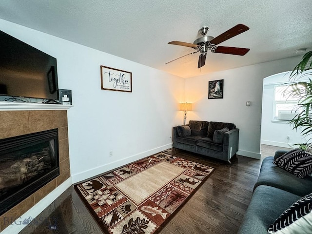 living room with ceiling fan, dark wood-type flooring, a fireplace, and a textured ceiling