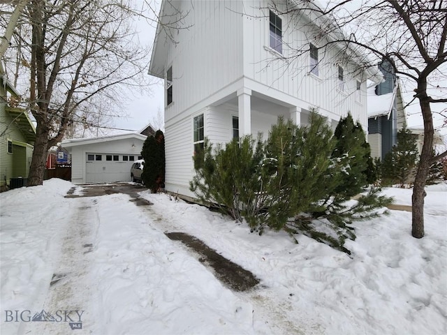 view of snow covered exterior featuring an outbuilding, a garage, and cooling unit