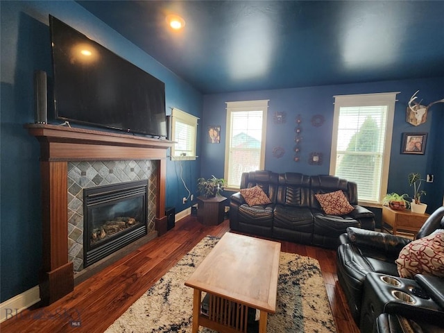 living room featuring a tile fireplace, a healthy amount of sunlight, and dark hardwood / wood-style flooring