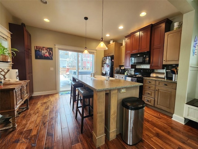 kitchen with an island with sink, sink, a kitchen breakfast bar, hanging light fixtures, and black appliances