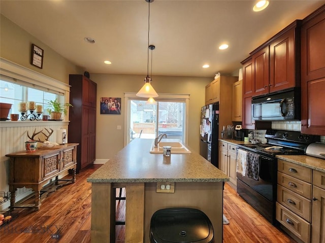 kitchen featuring decorative light fixtures, an island with sink, sink, black appliances, and light wood-type flooring