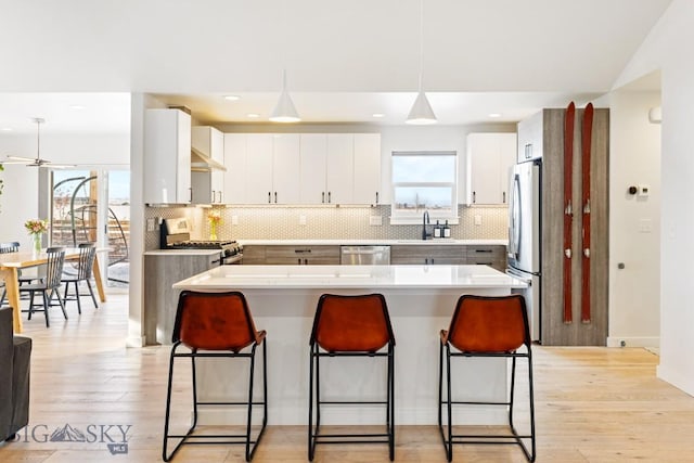 kitchen with sink, white cabinetry, light hardwood / wood-style flooring, appliances with stainless steel finishes, and pendant lighting