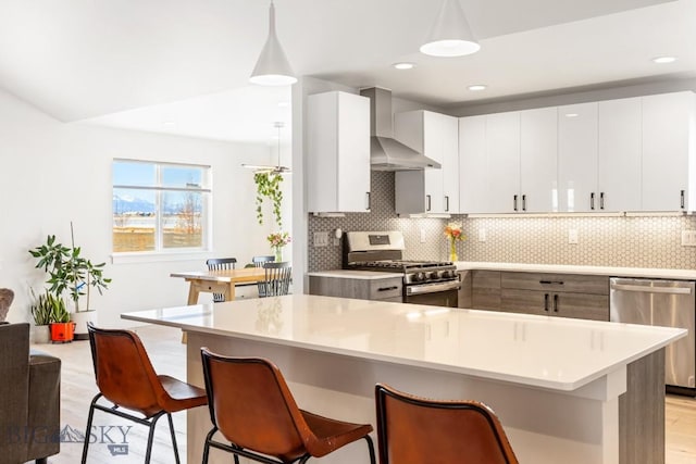 kitchen with decorative light fixtures, appliances with stainless steel finishes, wall chimney range hood, decorative backsplash, and white cabinets