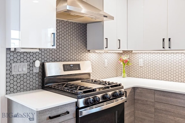 kitchen with wall chimney range hood, white cabinets, light countertops, gas range, and tasteful backsplash