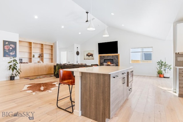 kitchen with a kitchen island, lofted ceiling, a breakfast bar area, a tiled fireplace, and light wood-type flooring