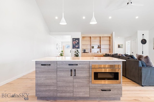 kitchen with stainless steel oven, decorative light fixtures, a center island, and light wood-type flooring