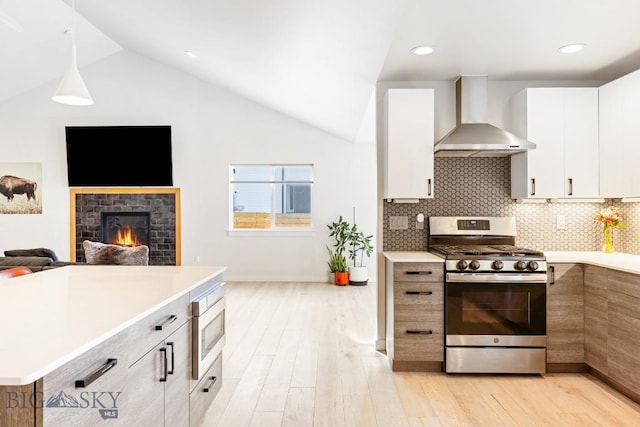 kitchen with wall chimney range hood, appliances with stainless steel finishes, hanging light fixtures, light hardwood / wood-style floors, and white cabinets