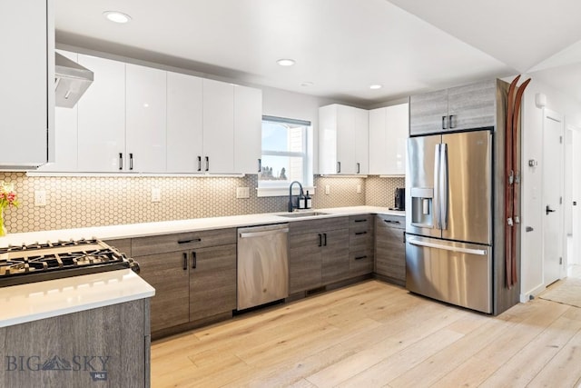 kitchen with white cabinetry, stainless steel appliances, sink, and light hardwood / wood-style flooring