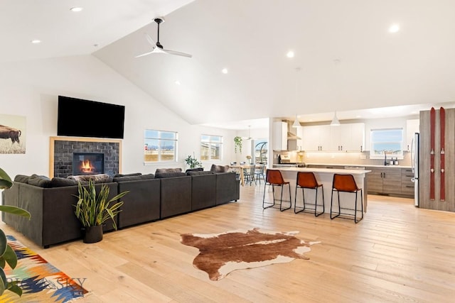 living room with ceiling fan, high vaulted ceiling, a fireplace, and light hardwood / wood-style floors